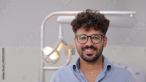 Handsome dark-haired American man with snow-white smile stands on the background of a dental office