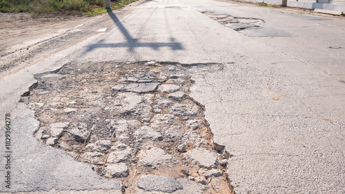 Damaged asphalt road with a large pothole and broken cracked surface, showing urban infrastructure deterioration and the need for maintenance and repair.