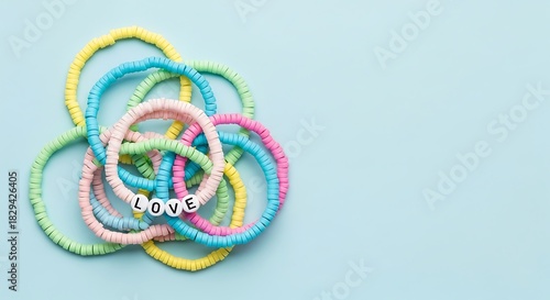 A colorful tangle of elastic hair ties, some featuring small white beads spelling out the word love, set against a light blue surface Background image