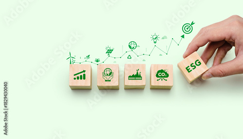 Wooden blocks displaying sustainability and ESG icons with a hand placing the ESG symbol, representing corporate responsibility, environmental impact, green growth, and sustainable strategy