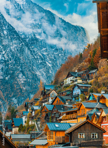 Hallstatt's beautiful wooden houses cling dramatically to a steep Alpine slope, crowned by towering, mist-covered mountains with streaks of snow and vibrant autumn foliage.