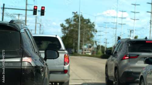 Rear side of black car with turn on brake light. Stop on concrete road by traffic red light control. Many car stop in junction road. Background of electric pole and trees at day in Thailand.