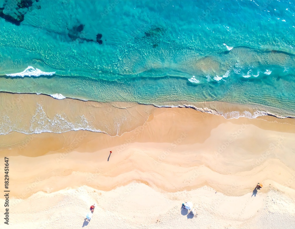 Obraz premium Aerial shot of a vibrant beach with turquoise waters meeting the sandy shoreline. One person is present
