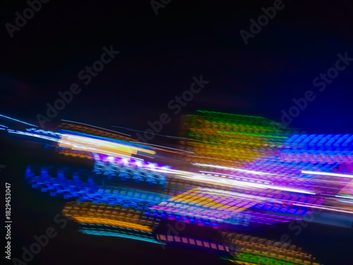An abstract image of bright light particles moving in the darkness of the night, creating a dynamic colorful trail of blue, yellow, and green.