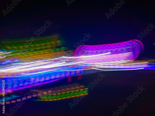 An abstract image of bright light particles moving in the darkness of the night, creating a dynamic colorful trail of blue, yellow, and green.