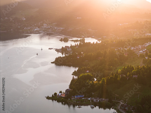 Aerial view of Colibița Lake in the Carpathian Mountains of Romania during a warm summer sunset. Golden light over the water and surrounding hills. Travel to Romania, Transylvania.