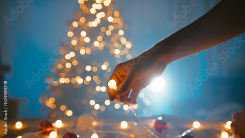 Hands of a boy arranging Christmas lights at night in front of the tree
