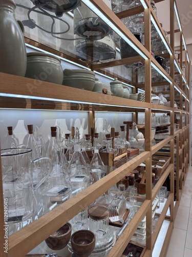 Glassware, ceramic dishes and home decor displayed on wooden shelves inside a Zara Home store. Modern retail interior, minimalist design, organized home accessories section. 