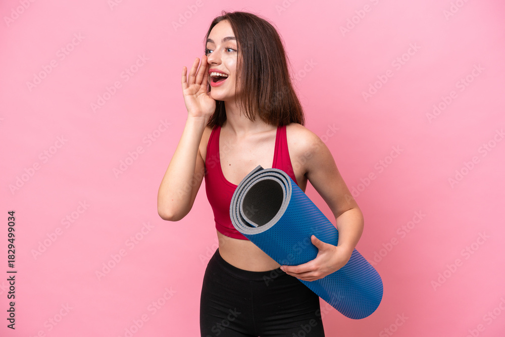 Obraz premium Young sport Ukrainian woman going to yoga classes while holding a mat isolated on pink background shouting with mouth wide open to the side