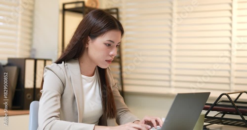 Asian businesswoman sitting at desk pressing temples with hands, feeling headache from stress and fatigue after long work hours, overworked employee suffering from mental exhaustion in office