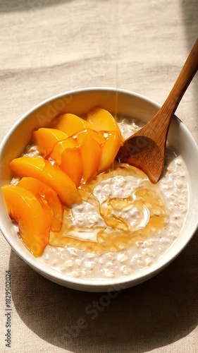 Close up shot of sweet honey being poured onto a bowl of creamy morning oatmeal topped with fresh ripe peach slices A healthy and delicious breakfast