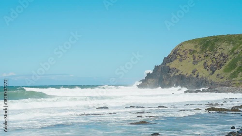 Slow motion, under the blue sky, waves crash against the cliffs creating huge splashes