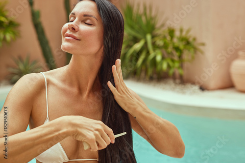 Close-up of a woman brushing smooth long hair outdoors during a natural hair care routine. Healthy shiny hair, summer beauty, wellness and tropical lifestyle concept.