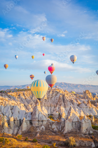 A stunning sunrise landscape in Cappadocia, Turkey, showcasing colorful hot air balloons drifting above the region’s iconic fairy chimneys and dramatic rock formations