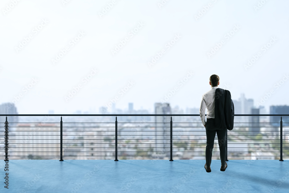 Obraz premium Businessman standing on rooftop terrace looking at city skyline in distance with a contemplative expression and jacket over shoulder.