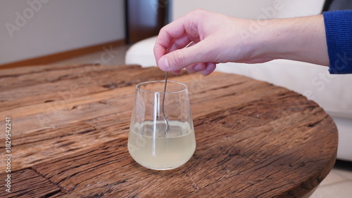 Tableau sur toile A hand stirring dissolved medicine in a glass of water on a rustic wooden table, concept of health, treatment, and home remedy