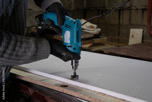 osoba w rękawicach ochronnych wierci otwór wiertarką w płycie wiórowej