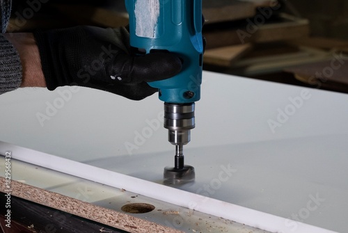 osoba w rękawicach ochronnych wierci otwór wiertarką w płycie wiórowej
