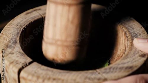 Close-up of wooden mortar and pestle crushing fresh green herbs for cooking or natural remedies