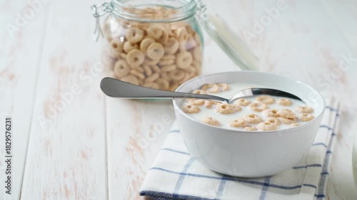 crispy cereal loops in a ceramic bowl on a white wooden table. Making a healthy breakfast using crispy cereal loops and milk.