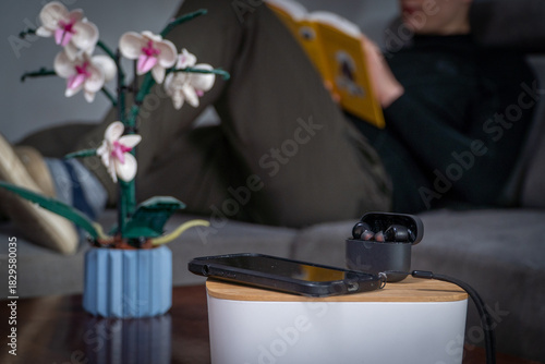 Smartphone and headphones set aside in the foreground while a man reads a book in the background. Concept of digital detox, disconnecting from technology, and returning to analog leisure