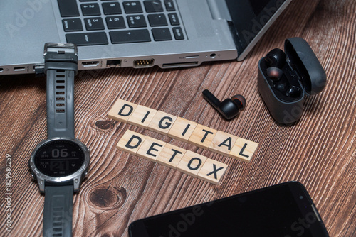 Flat lay composition featuring a Digital Detox sign surrounded by a smartphone, headphones, and laptop. Concept of unplugging, reducing screen time, and mental health awareness
