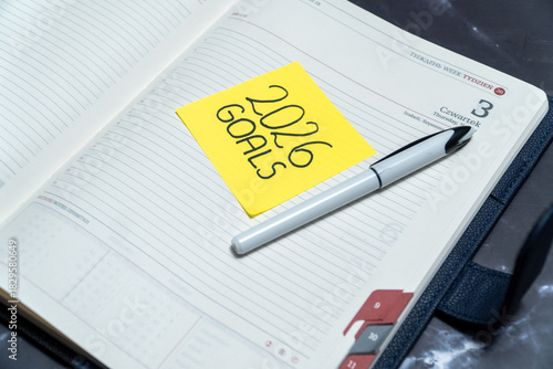 Note with text 2026 Goals placed on a book planner. Concept of New Year resolutions, strategic planning, motivation, and setting new objectives for the future