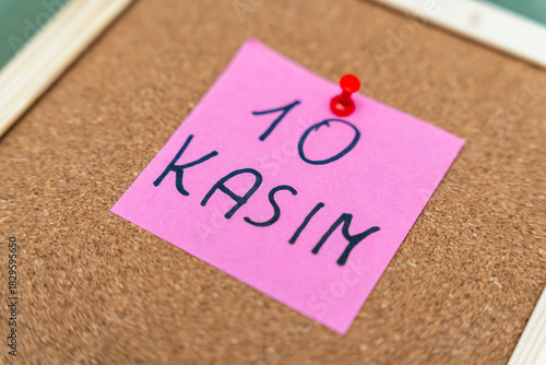 A pink sticky note pinned to a corkboard displays the handwritten date 10 Kasim, signifying an important reminder or event. The background is neutral, enhancing the note's visibility.
