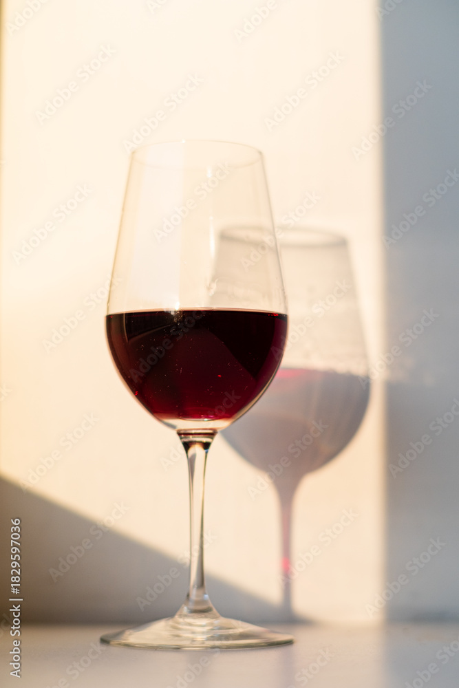 Fototapeta premium A beautifully filled glass of red wine stands tall, surrounded by gentle light and shadows