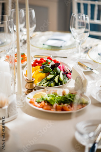 Plates of fresh fruits and vegetables are beautifully displayed on a dressed table with candles