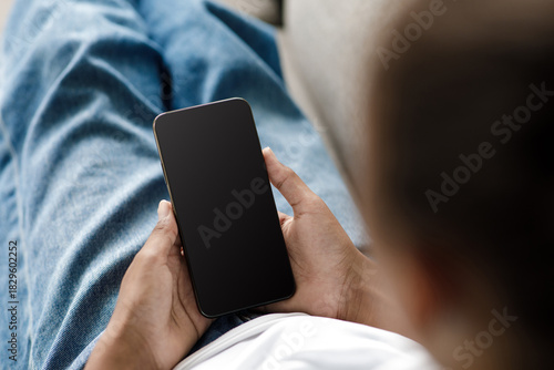 Tableau sur toile Young black girl sits comfortably on a sofa at home, focused on her smartphone