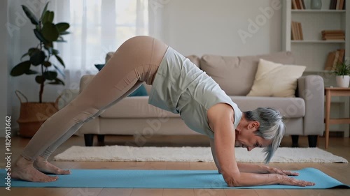 Flexible senior woman with gray hair doing yoga on a mat in her living room. Active elderly person exercising for health and wellness