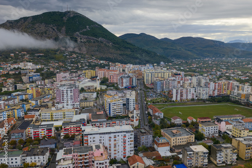 Aerial view of Lezhë with colourful residential blocks and Skanderbeg’s Tomb Peak rising above under cloudy skies.