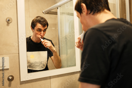 A man brushes his teeth while looking into the bathroom mirror. The moment represents personal hygiene and the concept of a healthy morning ritual.