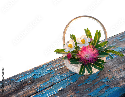 Small woven basket filled with white and pink flowers resting on rustic wooden surface with peeling blue paint outdoors