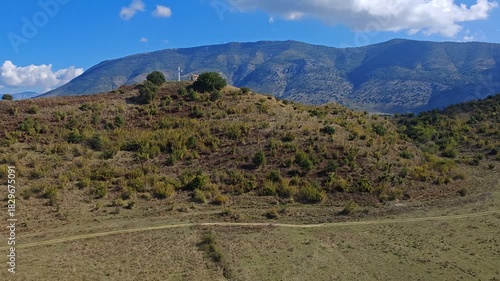 Aerial panorama of Albania mountains featuring a small hilltop Christian chapel with a prominent cross, set amid rugged terrain and sweeping natural vistas near Butrint