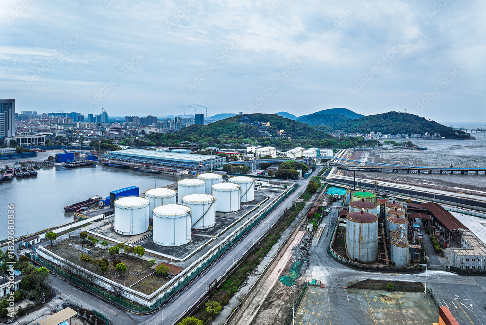 Obraz premium Aerial view of a coastal oil depot with storage tanks and long pier pipeline.