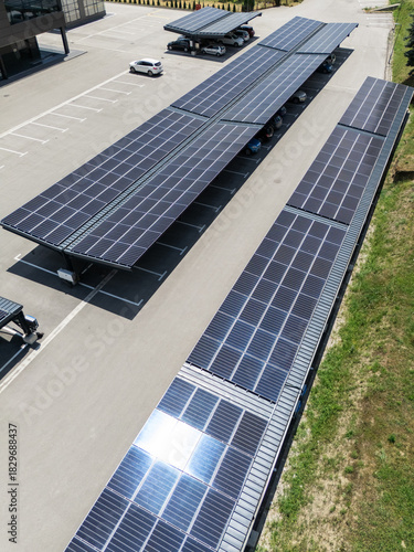 Aerial view of building with solar panels on a roof and parking space with solar canopies