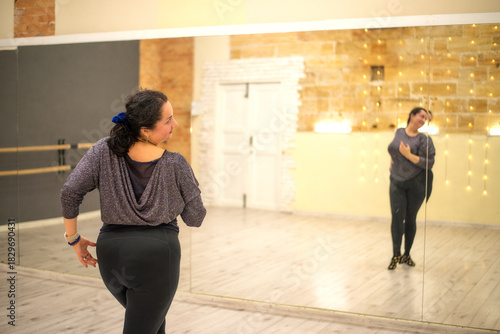 A confident plus-size woman practices expressive dance movements in a studio, embracing body positivity and freedom while training in front of large mirrors.