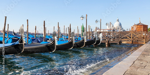 Row of gondolas moored in Bacino San Marco at Acqua Alta high tide with focus to the prows or Fero da Prora, Venice, Veneto, Italy, panorama banner