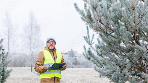 Mature man ecologist in winter forest, monitors the environment of a winter forest. Spruce trees to order. Observing animals and birds in a snowy forest. Nature and ecology conservation during winter.