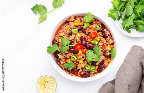 Spicy beef chili con carne with red beans, sweet corn, fresh cilantro, jalapeno pepper and tomato, served on white table, top view