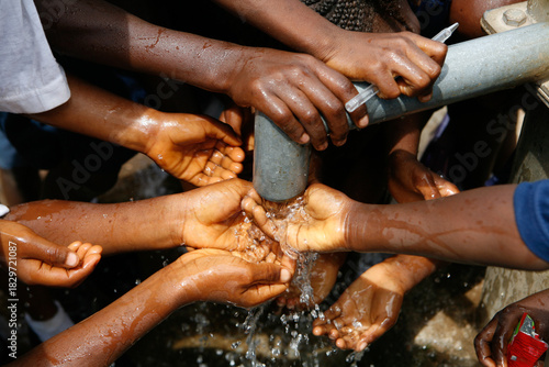 School with a biro pen and children's hands and water drops splashing beneath a running water tap in a West African village as they drink the clean water from a bore hole