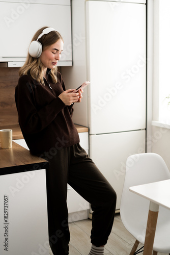 Woman in headphones listening music audio and relax in the kitchen. mobile app for listening to music at home.