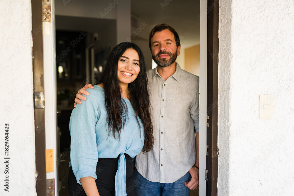 Naklejka premium Couple welcoming guests at front door, smiling happy at apartment entrance, husband and wife standing together at home