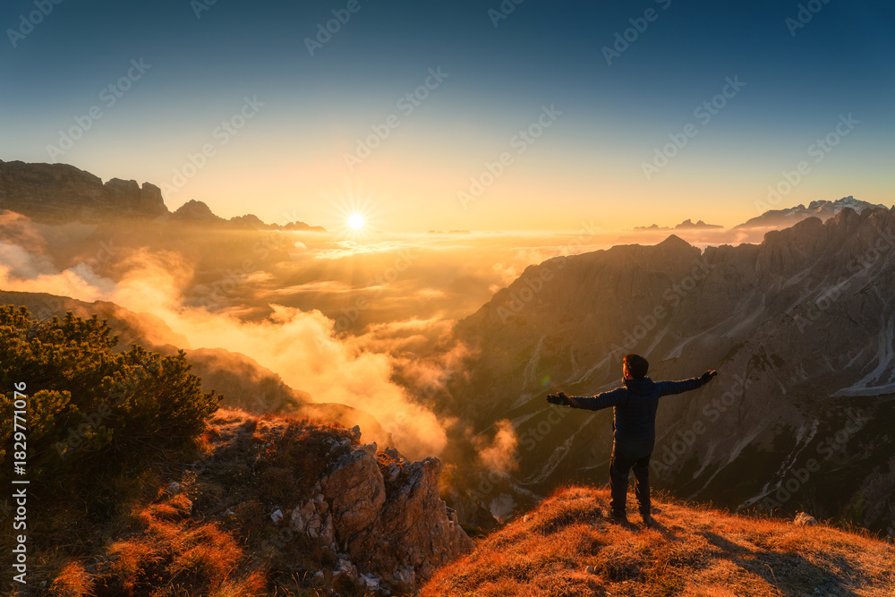 Fototapeta premium Majestic view of male tourist standing with sunrise over mountain ridge in Cadini di Misurina, Dolomites, Italy