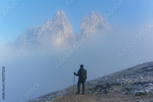 Hiker standing in dense fog facing dramatic Tre Cime mountain peak in Dolomites, Italy