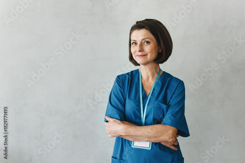 Portrait of smiling, confident Caucasian woman doctor wearing blue uniform and badge, isolated on gray copy space studio background. Happy healthcare professional, medicine, clinic concept