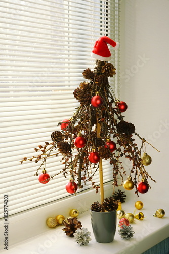  Decorations for the New Year holiday. Mini Christmas tree handmade from branches and pine cones decorated red and gold balls. Alternative Christmas decor on the windowsill.