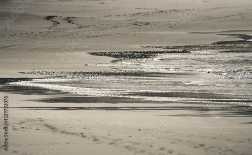 footprints on the beach and sea water with bubbles on wet white sand showing swash and backwash on the shore background or backdrop 
